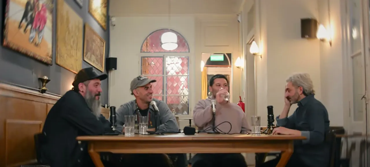 Cuatro hombres conversan con micrófonos alrededor de una mesa de bar