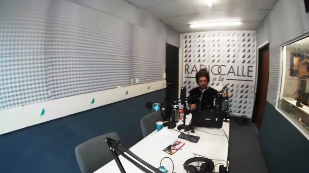 El estudio de Radio a la Calle: una mesa con micrófonos y, al fondo, el cartel con pájaros